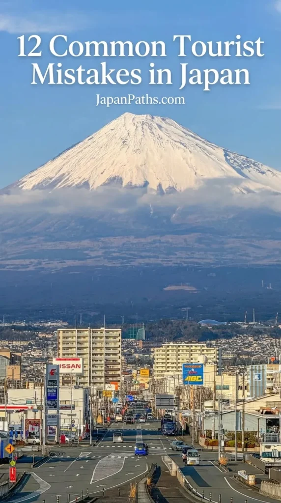 12 Common Tourist Mistakes in Japan: A stunning vertical shot of a long city street in Shizuoka with urban signs leading directly toward a massive, snow-capped Mount Fuji under a clear blue sky.